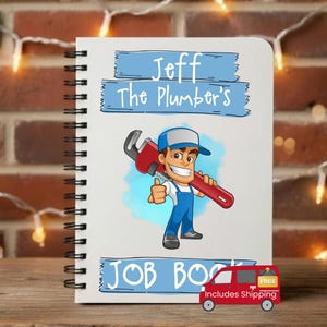 May include: A spiral-bound notebook with a cartoon plumber graphic. The notebook cover features the text "Jeff The Plumber's JOB BOOK" in blue banners. The cartoon plumber is holding a red wrench and giving a thumbs up.