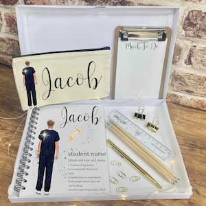 May include: A white gift box with a white background. The box contains a white pencil case with the name "Jacob" printed on it, a white notebook with the name "Jacob" printed on it, a white clipboard with the words "Much To Do" written on it, and a variety of stationery supplies. The notebook has a definition of "student nurse" printed on it.