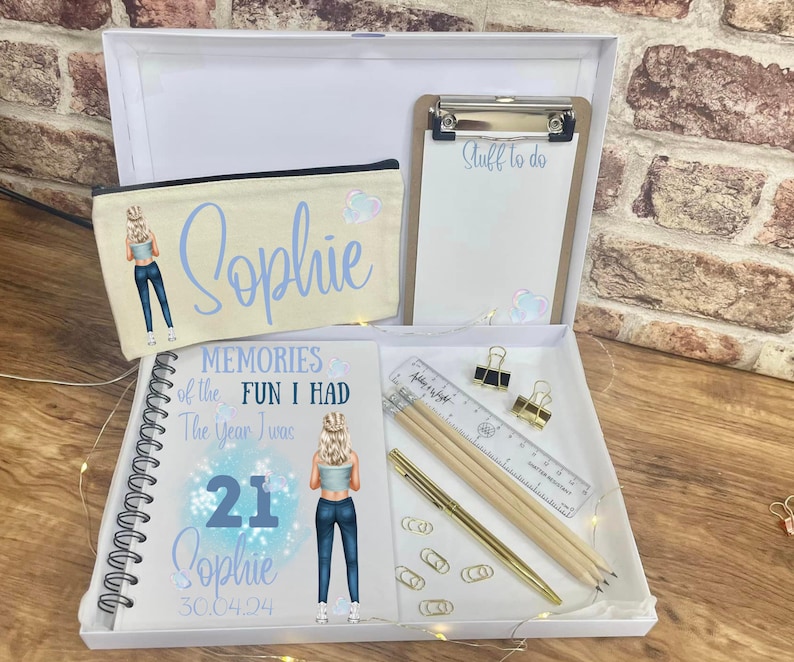 May include: A white gift box containing a pencil case, notebook, clipboard, and stationery. The pencil case and notebook feature a cartoon illustration and the name "Sophie". The notebook reads "Memories of the Fun I Had The Year I Was 21 Sophie 30.04.04".