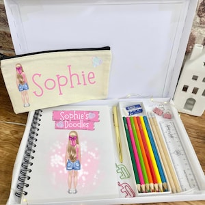 May include: A white box set containing a notebook, pencil case, and stationery. The notebook and pencil case feature a cartoon girl illustration and the name "Sophie". The set includes colored pencils, a pen, a ruler, and paper clips.