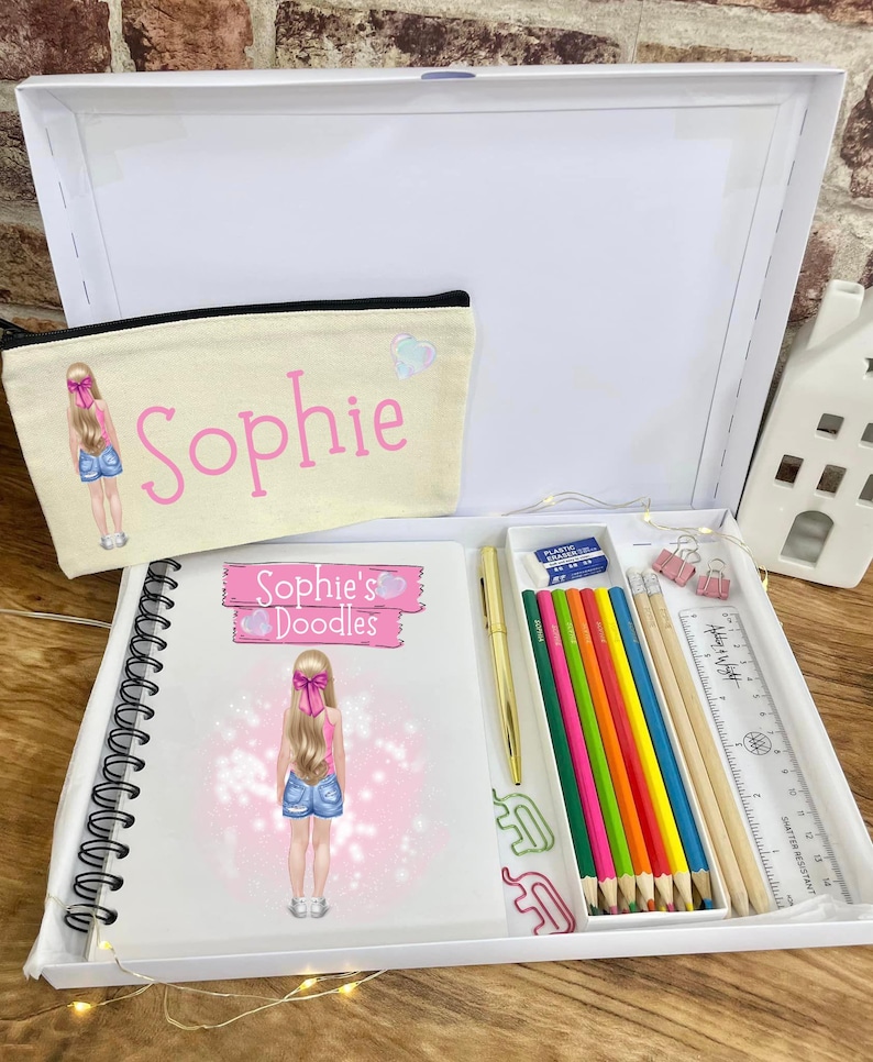 May include: A white box set containing a notebook, pencil case, and stationery. The notebook and pencil case feature a cartoon girl illustration and the name "Sophie". The set includes colored pencils, a pen, a ruler, and paper clips.