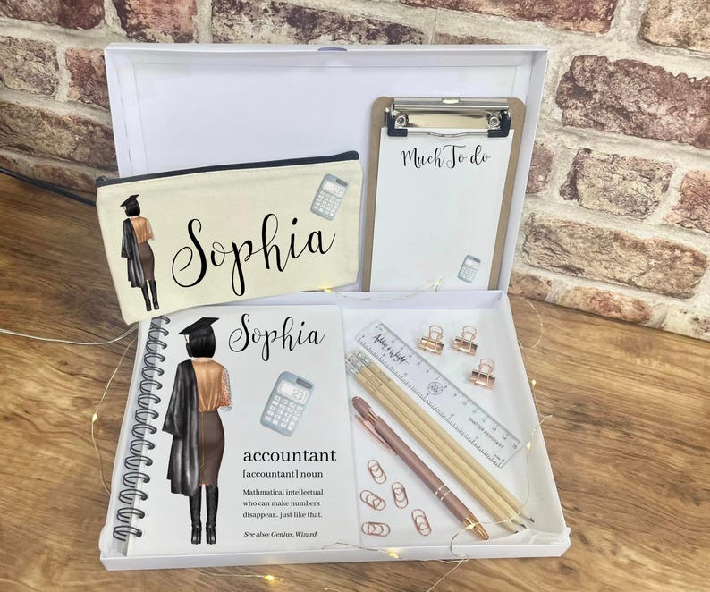 May include: A white gift box containing a pencil case, notepad, clipboard, and stationery. The pencil case and notebook feature the name "Sophia" and an illustration of a graduate. The clipboard reads "Much To Do". Includes pencils, a ruler, paper clips, and a pen.