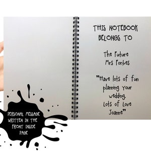 May include: A spiral-bound notebook with a white interior page featuring black printed text that reads: THIS NOTEBOOK BELONGS TO The Future Mrs Forbes Have lots of fun planning your wedding. Lots of Love Joanne. A black ink splatter graphic is included.