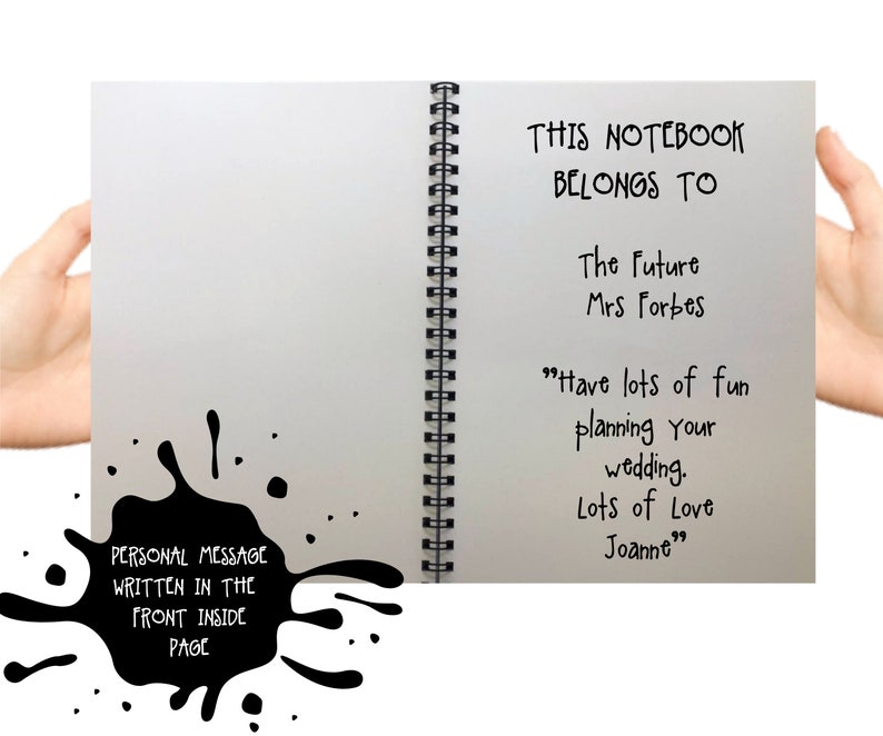 May include: A spiral-bound notebook with a white interior page featuring black printed text that reads: THIS NOTEBOOK BELONGS TO The Future Mrs Forbes Have lots of fun planning your wedding. Lots of Love Joanne. A black ink splatter graphic is included.