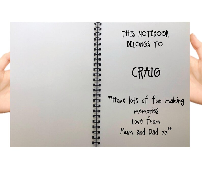 May include: A white notebook with a black spiral binding. The front cover has the text "THIS NOTEBOOK BELONGS TO CRAIG" and the message "Have lots of fun making memories Love from Mum and Dad xx".