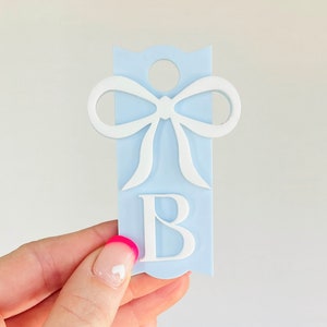 May include: A light blue gift tag with a white bow and the letter "B" in white. The tag has a hole at the top for hanging.