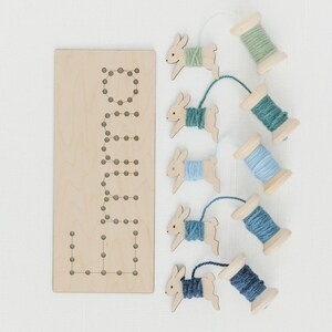 May include: Wooden bunny shaped lacing cards with spools of yarn in shades of blue and green. The cards have holes for threading the yarn.