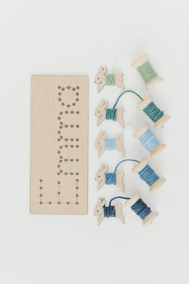 May include: Wooden bunny shaped lacing cards with spools of yarn in shades of blue and green. The cards have holes for threading the yarn.