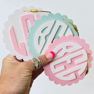 Puede incluir: Tres decoraciones de pared redondas con bordes festoneados, fondo blanco y monogramas rosa, azul claro y rosa oscuro. Los monogrammes son de estilo tradicional.