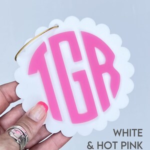 Puede incluir: Adorno circular blanco con festones con un monograma "TGR" rosa intenso en el centro.  BLANCO & ROSA INTENSO.