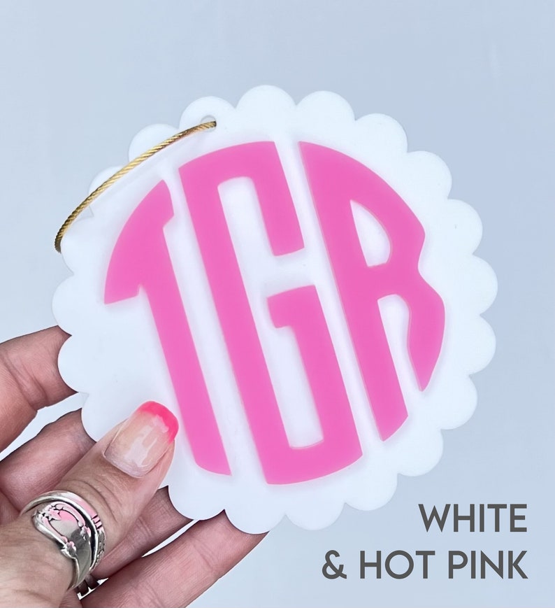 Puede incluir: Adorno circular blanco con festones con un monograma "TGR" rosa intenso en el centro.  BLANCO & ROSA INTENSO.