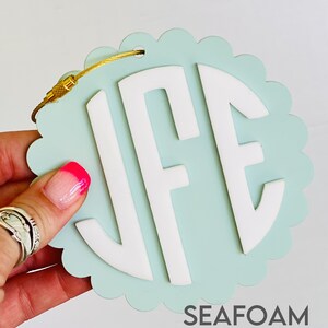 Puede incluir: Una etiqueta de equipaje azul claro con un monograma blanco "JFE" y una cadena dorada. La etiqueta tiene un borde festoneado y el texto "SEAFOM & WHITE" est&aacute; impreso debajo del monograma.