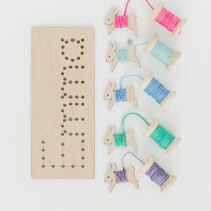 May include: Wooden bunny shaped lacing cards with colorful yarn spools. The card has the word "Bunny" spelled out with holes for lacing.