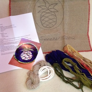 May include: A pineapple embroidery kit with a printed pattern, instructions, and a variety of colored embroidery floss. The kit includes a piece of burlap fabric with a pre-printed pineapple design and the text "Spears 2012".