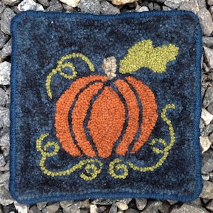 May include: A square, hand-stitched rug featuring an orange pumpkin with a green leaf and yellow vines on a dark blue background. The pumpkin is the central focus, with a textured appearance. The rug has a dark blue border.
