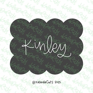 May include: A dark gray, scalloped-edge design with the name "Kinley" in white cursive script. The design includes the text "@KaleidaCuts 2025" at the bottom, suggesting a custom product or template.