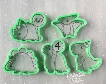 May include: Set of five green plastic dinosaur cookie cutters. The cutters are shaped like a triceratops, a pterodactyl, a stegosaurus, a brachiosaurus, and a T-Rex. The brachiosaurus is holding a balloon that says "4" on it. The triceratops is holding a balloon that says "RAWR" on it. The T-Rex is wearing a party hat.