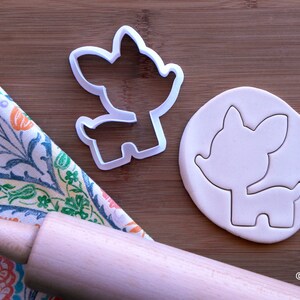May include: White plastic cookie cutter shaped like a cartoon deer. The cutter is shown next to a piece of white fondant with the deer shape cut out.