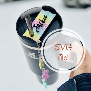 May include: A black travel mug with a colorful tie-dye sticker that says "Jackie" on it. The mug has a silver chain with colorful flower charms attached. The image includes the text "SVG file!" in a white circle.