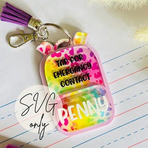 May include: A pink backpack-shaped keychain with a colorful leopard print design. The keychain has the text "TAP FOR EMERGENCY CONTACT" and "PENNY". It includes a purple tassel and a silver clasp.