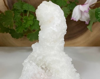 Op de afbeelding: Een witte en roze kristalkluster met een unieke, organische vorm. De kristal is een natuurlijke formatie met een ruw, getextureerd oppervlak.