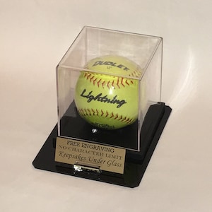 May include: A yellow softball with red stitching and the word "Lightning" written on it is displayed in a clear acrylic display case with a black base. The base has a gold plaque that reads "FREE ENGRAVING NO CHARACTER LIMIT Keepsakes Under Glass".
