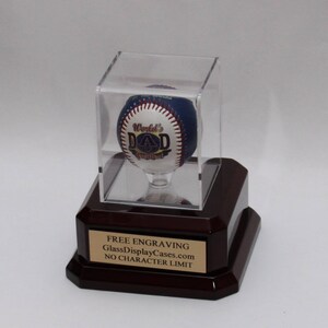 May include: A baseball with the words "World's Greatest Dad" on it is displayed in a clear acrylic case on a mahogany base. The base has a gold plaque that reads "FREE ENGRAVING GlassDisplayCases.com NO CHARACTER LIMIT".