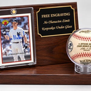 May include: A dark wood display plaque featuring a Don Mattingly baseball card in a clear protective case, a black engraved plate with the text "FREE ENGRAVING No Character Limit Keepsakes Under Glass," and a 2000 World Series baseball in a clear holder.