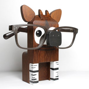 May include: Wooden eyeglasses holder shaped like a cartoon animal with brown fur, white eyes, and black stripes on its legs. The animal is wearing glasses.