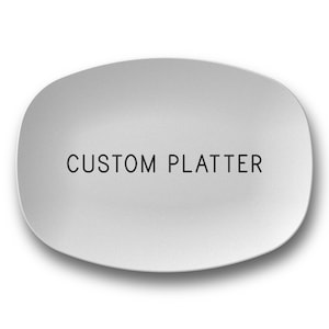 May include: A light gray, oval-shaped platter with rounded edges. The words "CUSTOM PLATTER" are printed in black, centered on the surface. The platter is likely ceramic or porcelain, with a smooth finish.