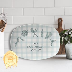 May include: An oval serving platter with a light blue and white checkered pattern. The platter features illustrations of barbecue food items and the text "THE ROBINSON FAMILY". A Honey Brush Design logo is in the lower left corner.