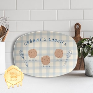 May include: An oval serving platter with a light blue and white gingham pattern. The words "Grammy's Cookies" are written in blue script. The platter features illustrations of cookies, a whisk, and a spatula, with names below the cookies.