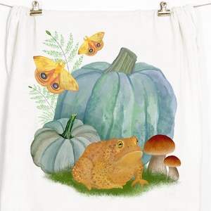 May include: A watercolor illustration of a toad, two pumpkins, two mushrooms, and two butterflies. The toad is orange and brown, the pumpkins are blue-green, the mushrooms are brown and white, and the butterflies are yellow with black eyes.