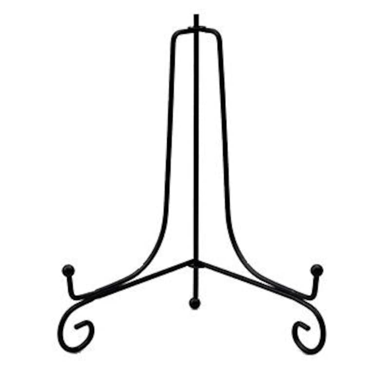 Puede incluir: Un soporte de exhibici&oacute;n de metal negro con un dise&ntilde;o curvo. El soporte tiene tres patas con adornos decorativos y un soporte superior para sostener objetos. Dise&ntilde;ado para platos, obras de arte u otros objetos decorativos.