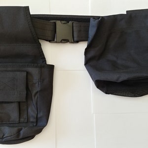 May include: Black canvas tool belt with two pouches and a black adjustable buckle. The belt has a mesh pocket on the bottom of one of the pouches.