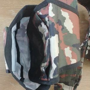 May include: Camouflage-patterned tool belt with multiple pockets and a black strap. The belt is made of a durable fabric and has a variety of compartments for storing tools.