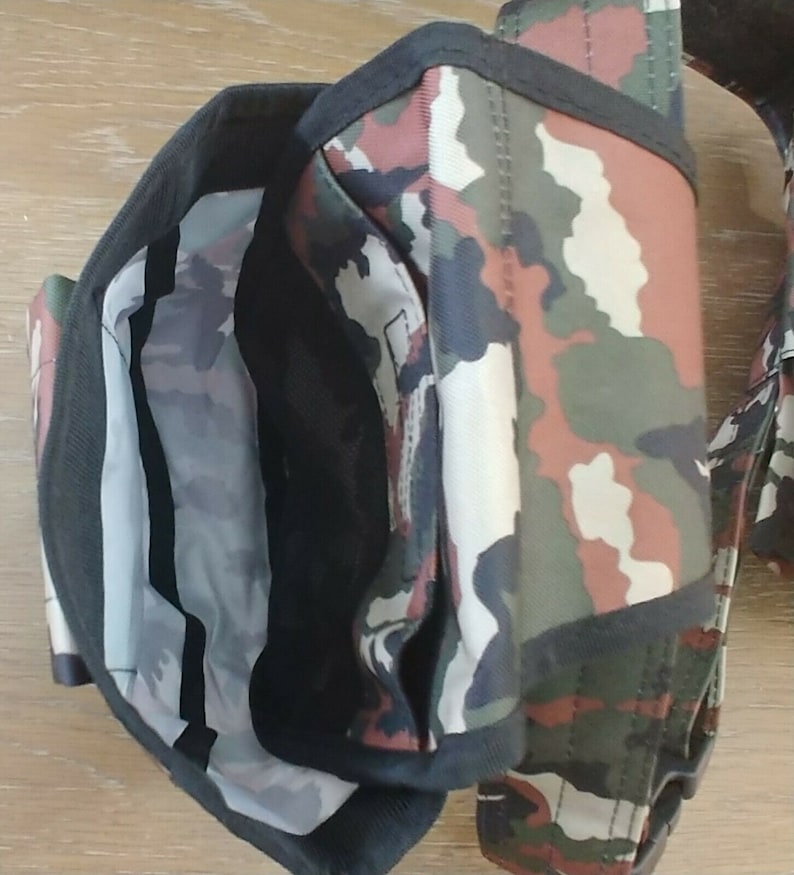 May include: Camouflage-patterned tool belt with multiple pockets and a black strap. The belt is made of a durable fabric and has a variety of compartments for storing tools.