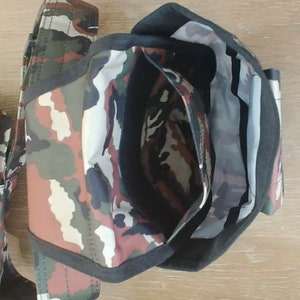 May include: A camouflage-patterned bag with a black zipper and a black strap. The bag is open and the inside is visible.