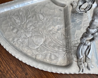 May include: A silver serving tray with a hammered finish and an embossed tulip design. The tray has a raised handle with a floral design.