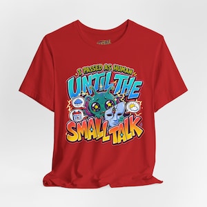 May include: A red t-shirt featuring a graphic of a green alien holding a cracked human face mask. The text reads I PASSED AS HUMAN UNTIL THE SMALL TALK, surrounded by icons of a rain cloud, a calendar, and a sun with a cloud in a comic style.