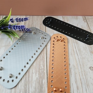 May include: Three leather bag strap base pieces in different colors: silver, copper, and black. Each piece has a rectangular shape with rounded edges and multiple holes for stitching.