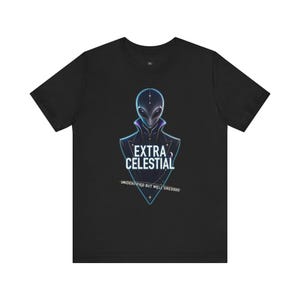 May include: A black short-sleeve t-shirt featuring a graphic of an alien wearing a high-collared jacket. The design includes the text "EXTRA CELESTIAL" and "UNIDENTIFIED BUT WELL DRESSED" in white lettering, framed by a blue triangular outline.