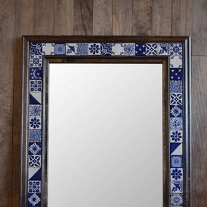 May include: A rectangular mirror with a dark brown wooden frame decorated with blue and white patterned tiles. The tiles are arranged in a border around the mirror.