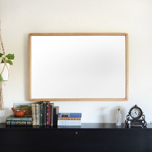 Puede incluir: Un piano negro con un espejo enmarcado en madera colgado encima. El piano tiene un teclado blanco y negro y las palabras "KAWAI" impresas en la parte delantera. Hay libros y un pequeño reloj en la estantería encima del piano.