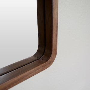 Puede incluir: Primer plano de la esquina de un espejo con marco de madera. El marco est&aacute; hecho de dos piezas de madera, creando un efecto de doble capa. La madera es de color marr&oacute;n oscuro.