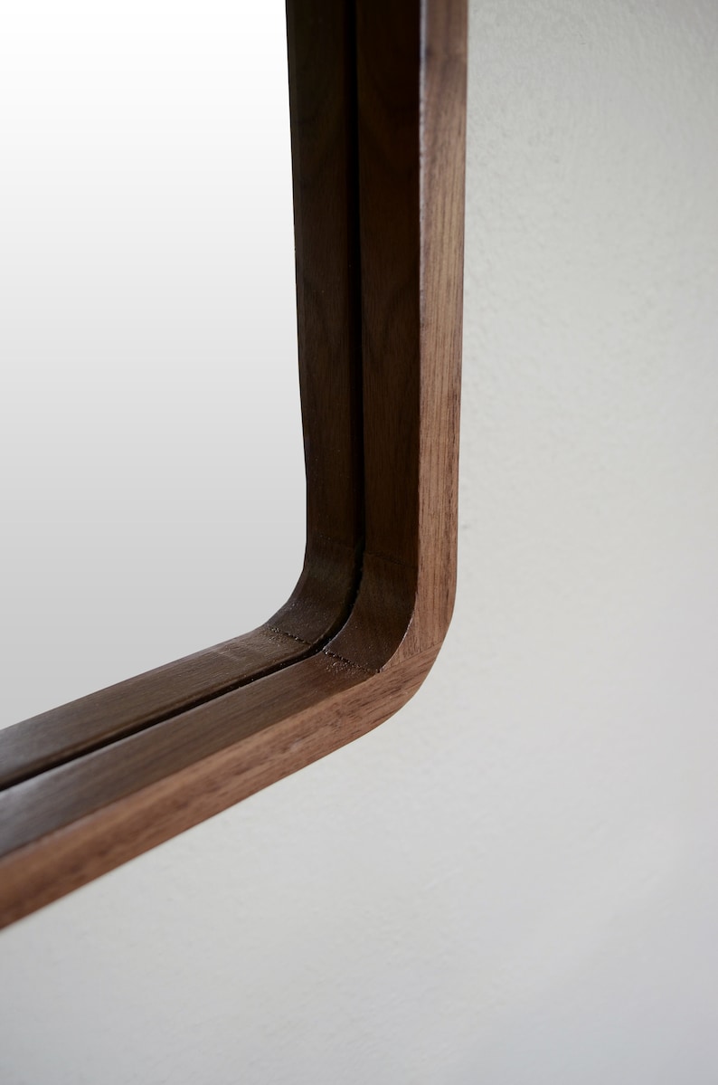 Puede incluir: Primer plano de la esquina de un espejo con marco de madera. El marco est&aacute; hecho de dos piezas de madera, creando un efecto de doble capa. La madera es de color marr&oacute;n oscuro.