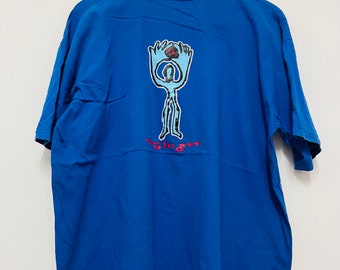 Può includere: Una t-shirt blu con una grafica di una persona stilizzata che tiene un globo rosso. Il testo "Volcom" è stampato sotto la grafica.