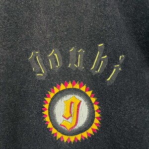 May include: Black sweatshirt with a yellow and pink sunburst design. The design features the letter "J" in a yellow and pink color scheme. The word "SOUL" is arched above the sunburst in yellow.