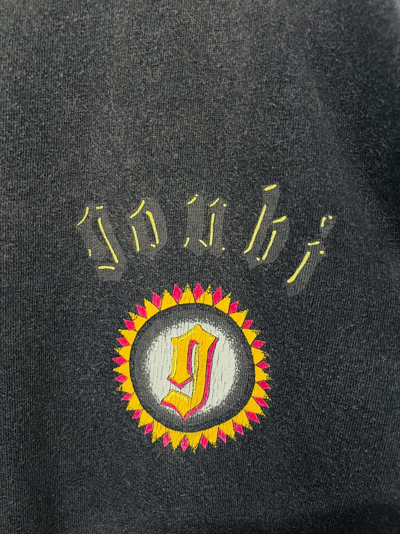 May include: Black sweatshirt with a yellow and pink sunburst design. The design features the letter "J" in a yellow and pink color scheme. The word "SOUL" is arched above the sunburst in yellow.