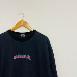 May include: Black t-shirt with a red and blue "plastik" logo printed on the front.